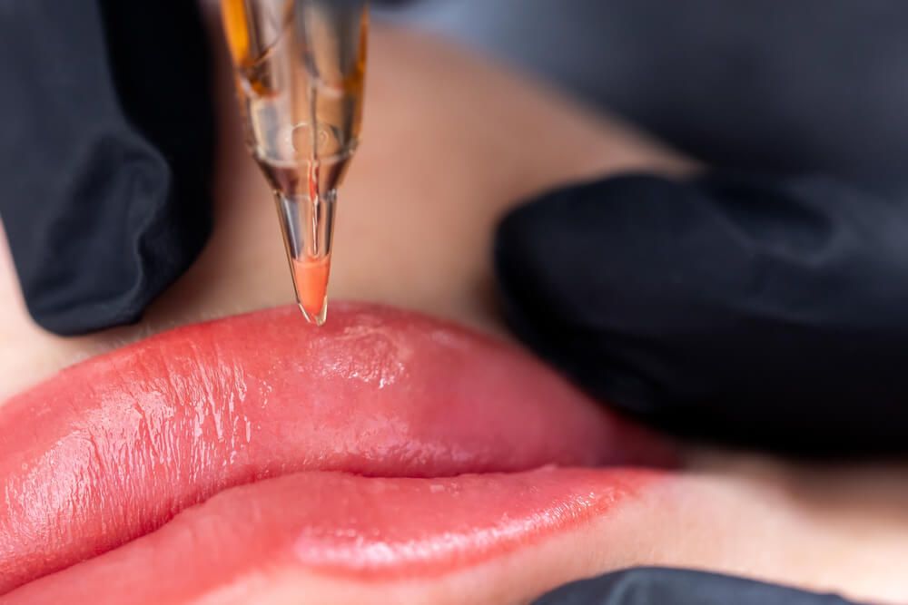 Macro photo of process of applying permanent makeup tattoo of red on lips woman