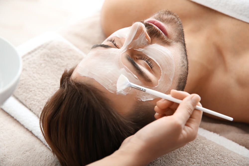 Cosmetologist applying mask on client's face in spa