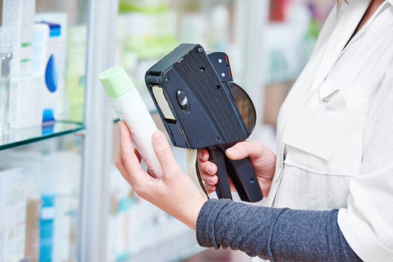 Hand of female pharmacist using labeling gun labeler for sticking price label of medicine in drugstore