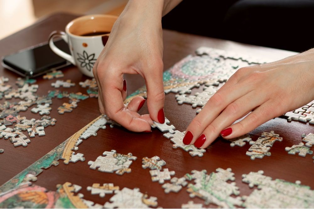 Woman hands with red nail polish putting jigsaw puzzle pieces together
