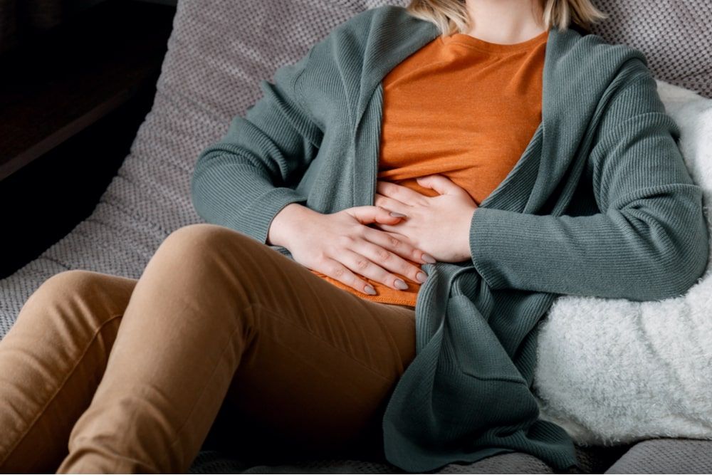 Young woman suffers, writhes in abdominal pain lying on couch
