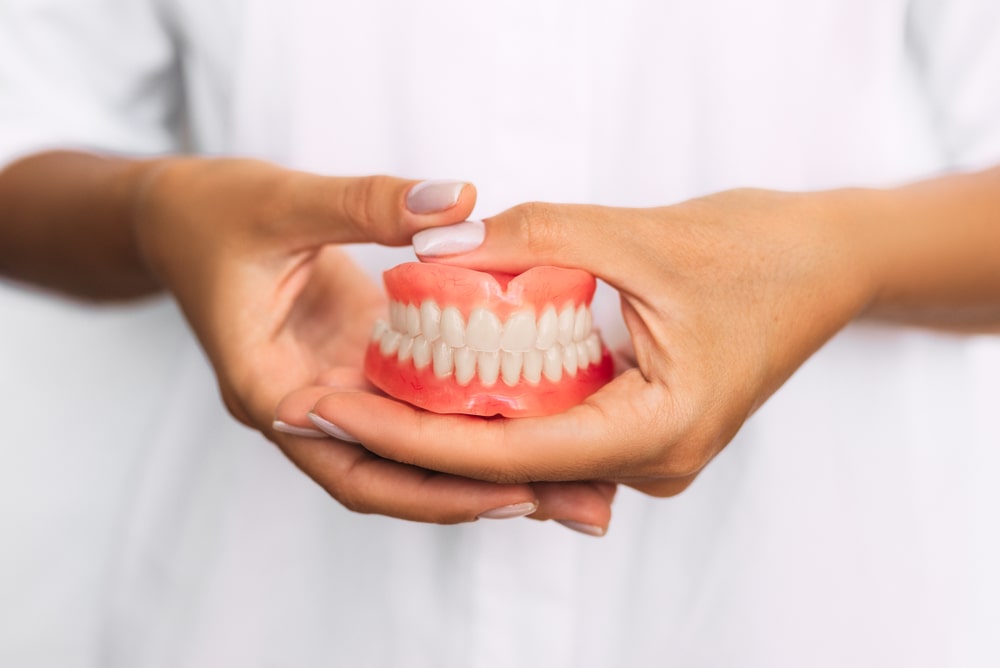 The dentist is holding dentures in his hands