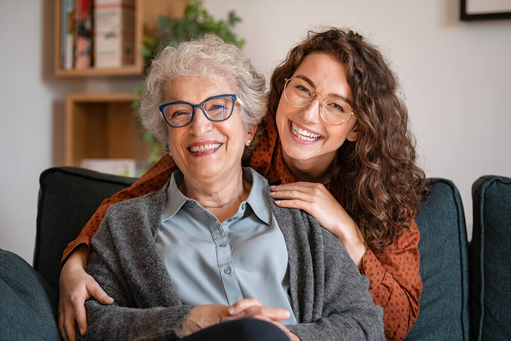 Portrait of old grandma and adult granddaughter hugging with love on sofa