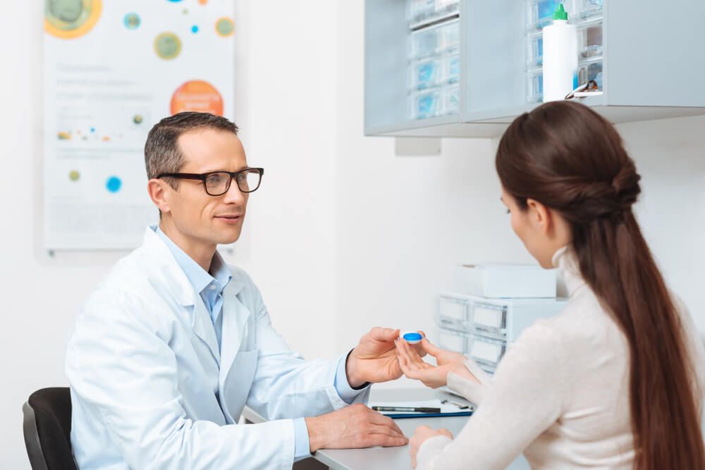 side view of ophthalmologist in eyeglasses giving contact lens to patient in clinic