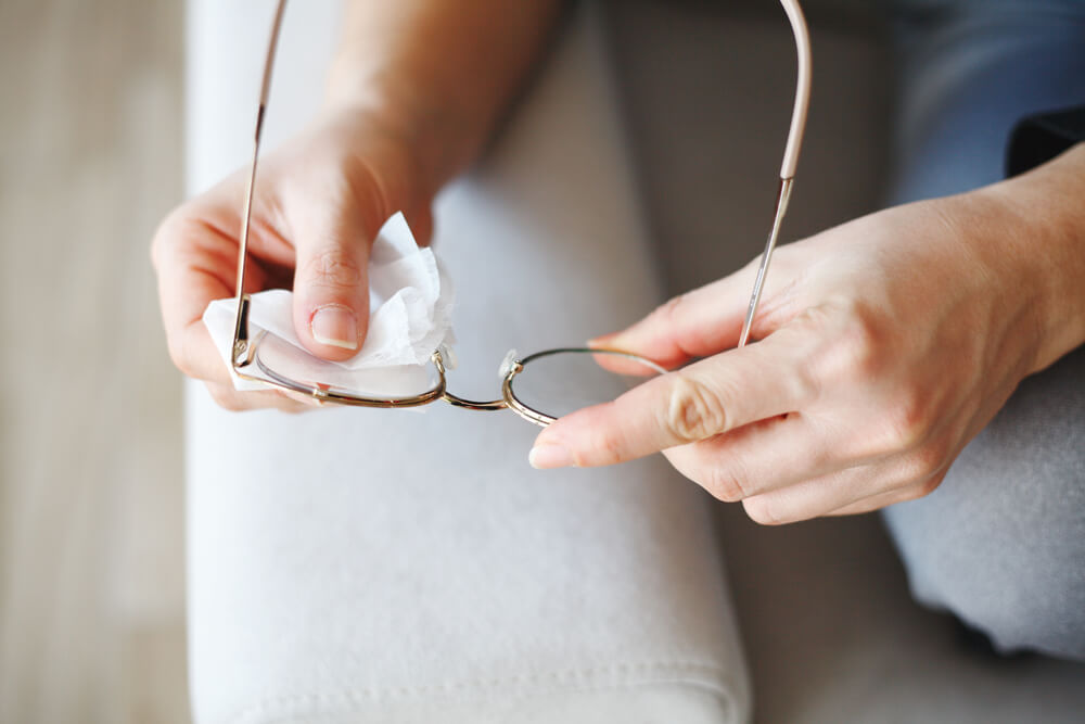 Hand wiping glasses with disinfectant wipes due to corona virus pandemic.