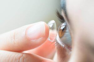 Young woman putting contact lens in her right eye