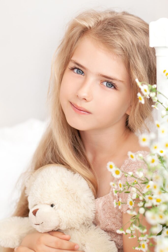 A close-up portrait of the face of a cute little girl hugs a teddy bear