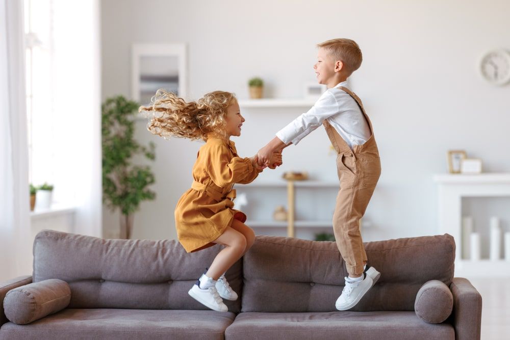 Full length of overjoyed little children brother and sister jumping on sofa