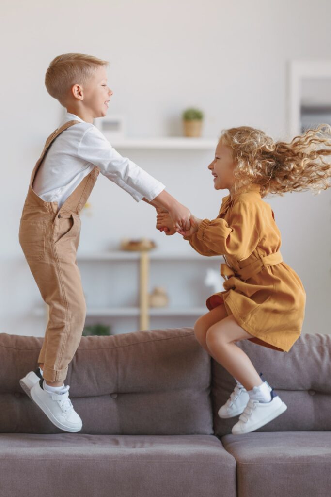 Full length of overjoyed little children brother and sister jumping on sofa