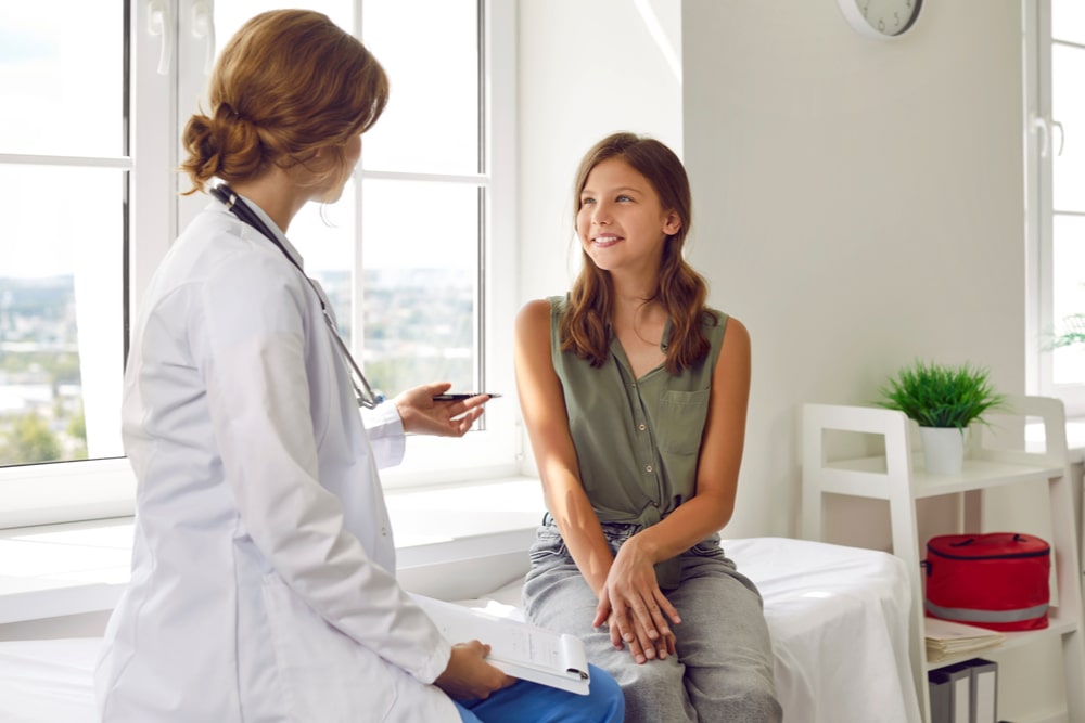 Happy teenage girl is listening to doctor during medical examination in modern clinic