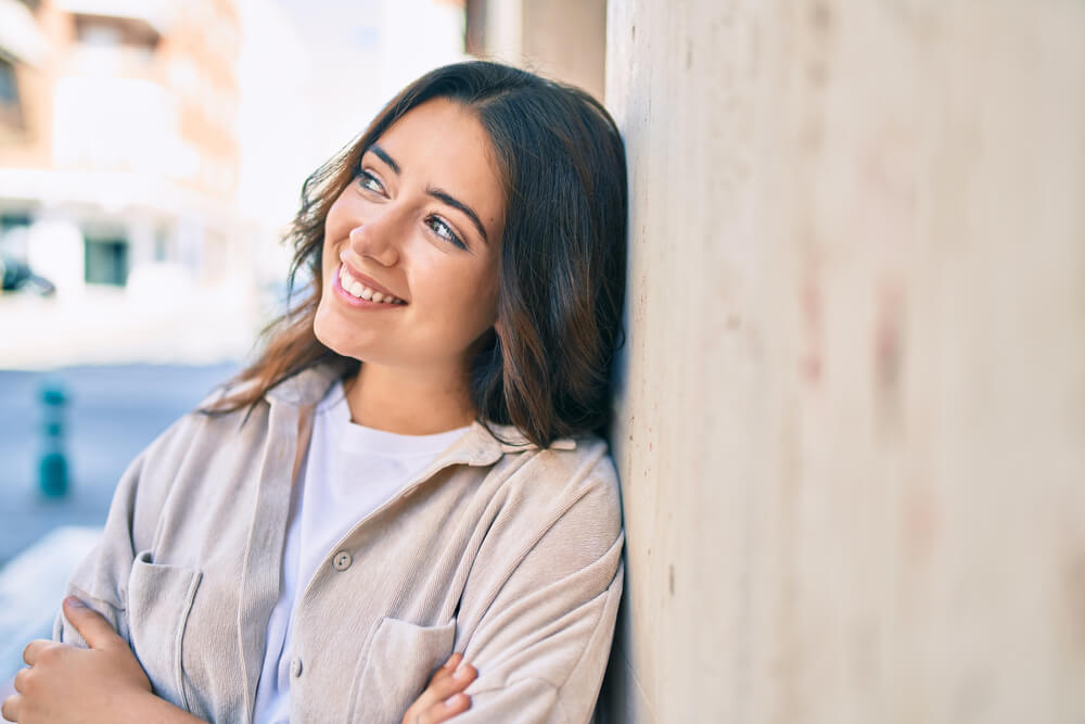 Young woman smiling happy leaning on the wall at the city.