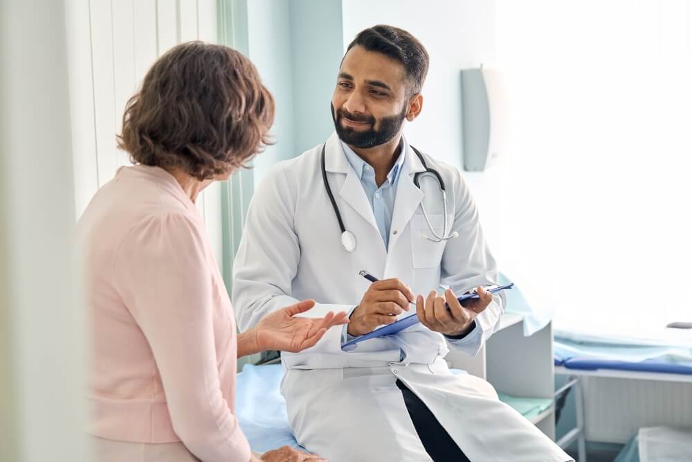 Indian male doctor consulting senior old patient filling form at consultation