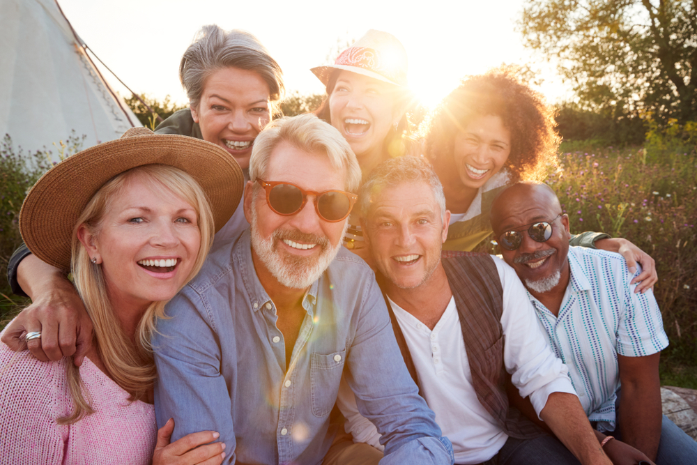 Portrait Of Mature Friends By Tent On Camping Vacation Against