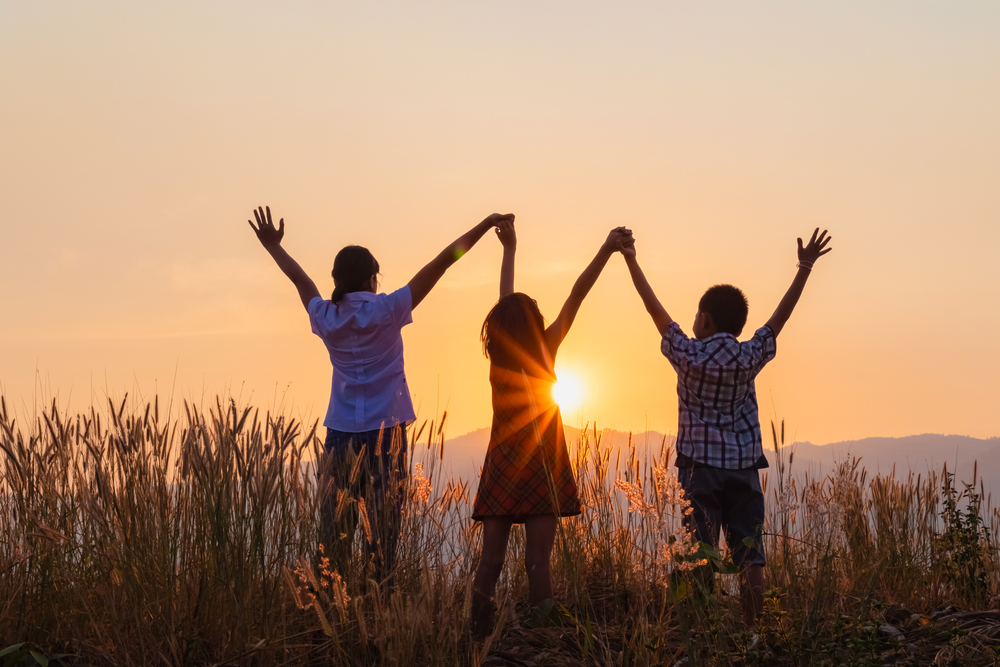 Silhouette Of Happy Children Standing With Raised Hands On The