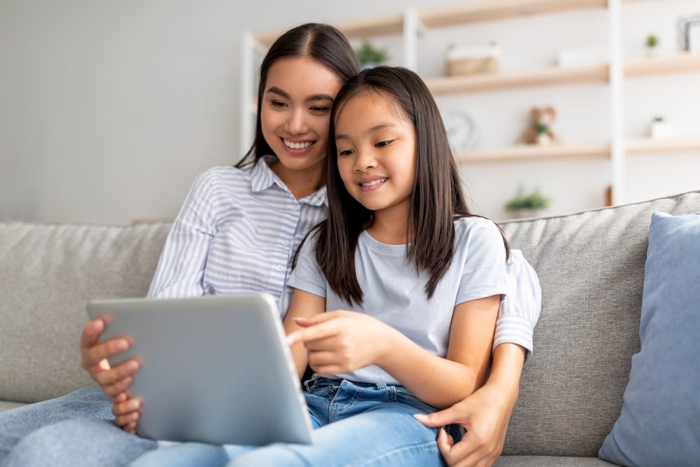 Happy mom and child playing online games on pad