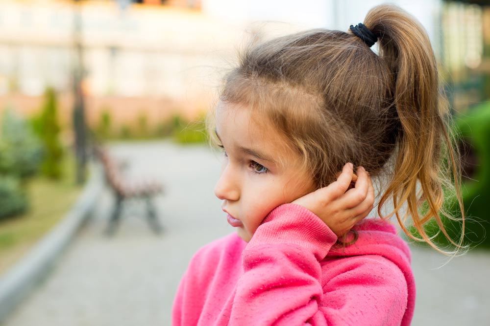 A little girl with a sad and frightened face holds her cheek with her hand