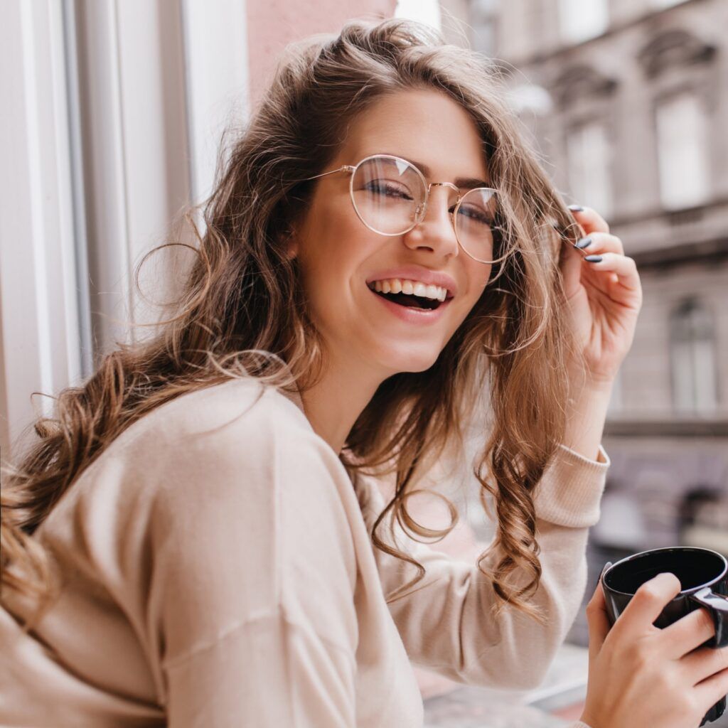 laughing brunette girl in beige sweater drinking coffee