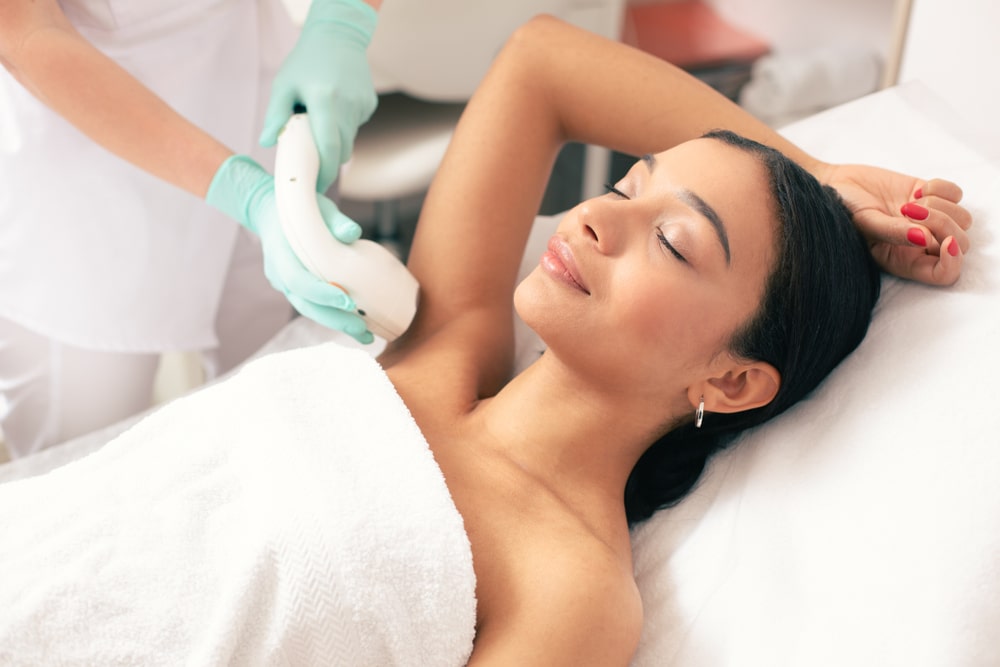 Woman lying with closed eyes and putting on arm up while having laser