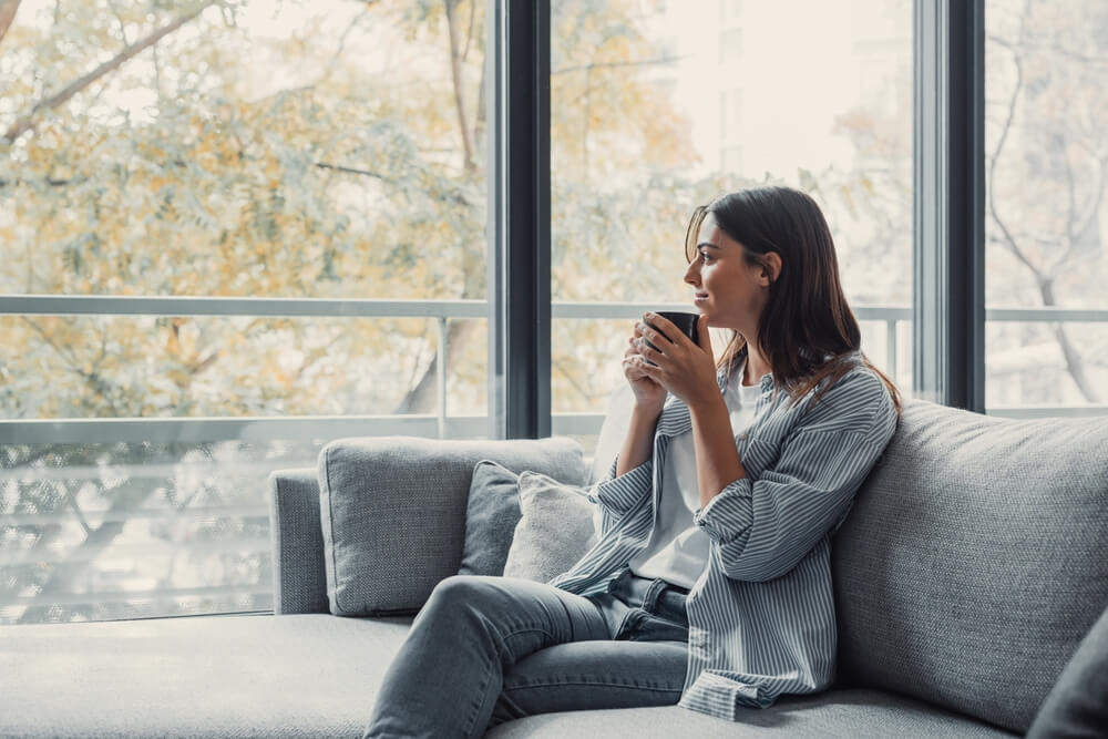 Cheerful dreamy girl holding mug of hot beverage,