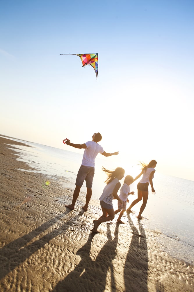 Happy young family with two kids with flying a kite on the beach