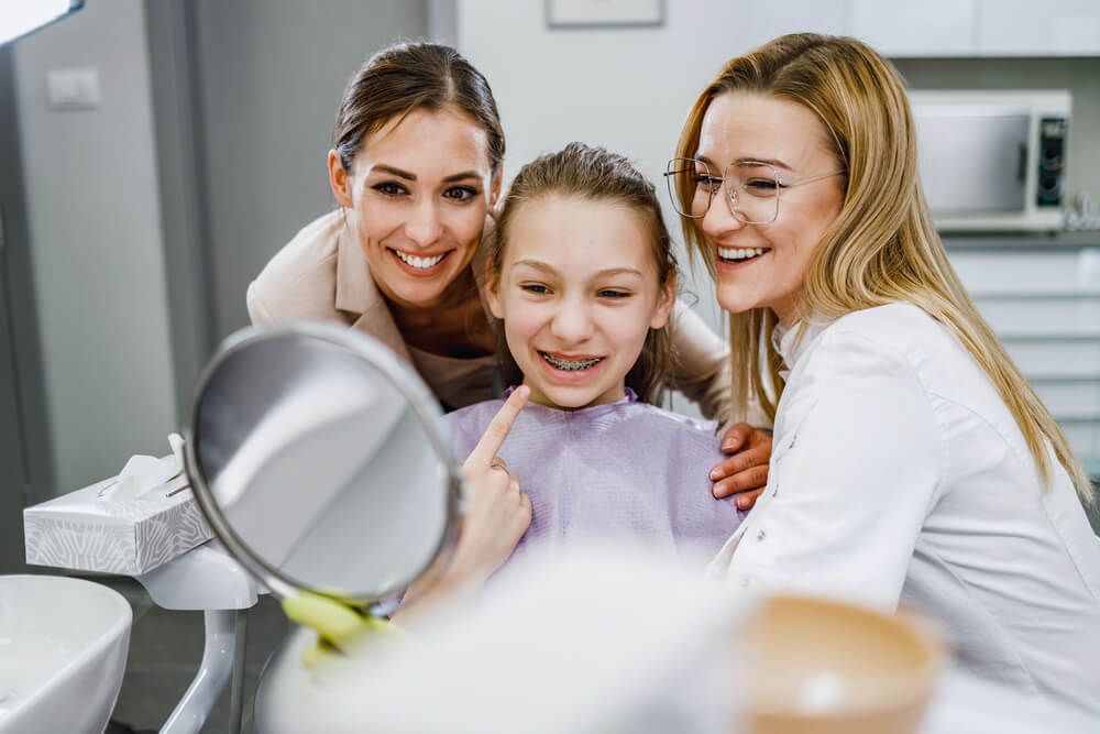 A happy teenager girl looking her teeth in a mirror after dental procedure