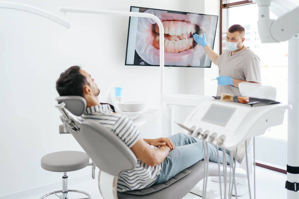 Dentist discussing with laying patient showing the image of his teeth on the screen