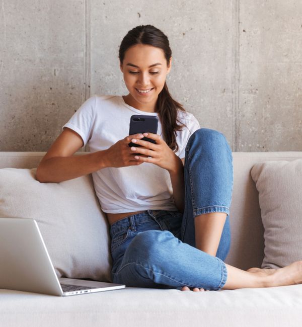 Happy young woman using mobile phone while sitting a couch