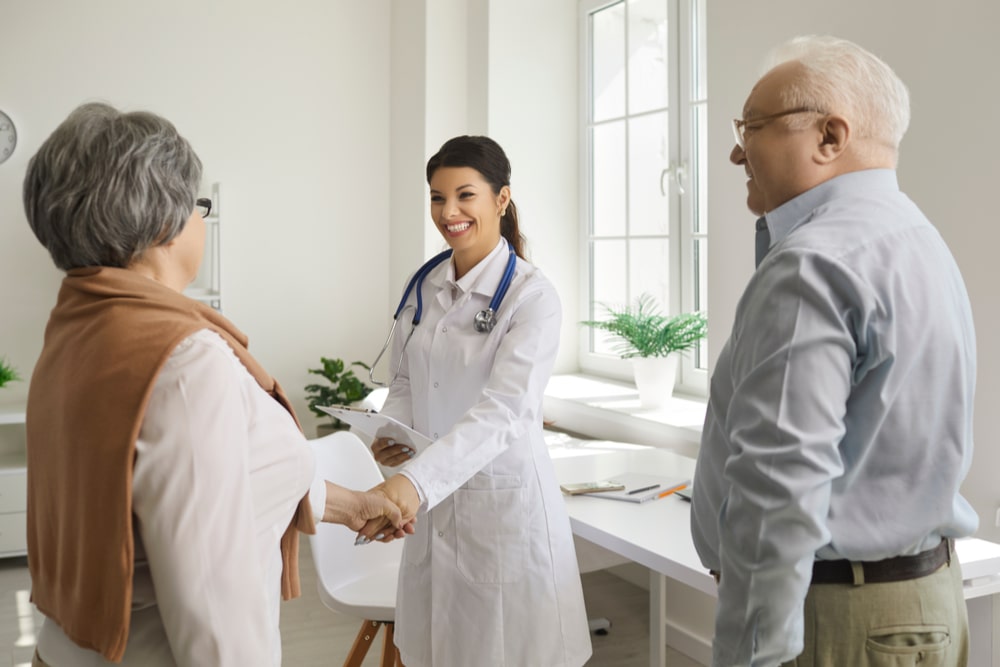 Female doctor shakes hands with an elderly woman who came to the clinic with her husband