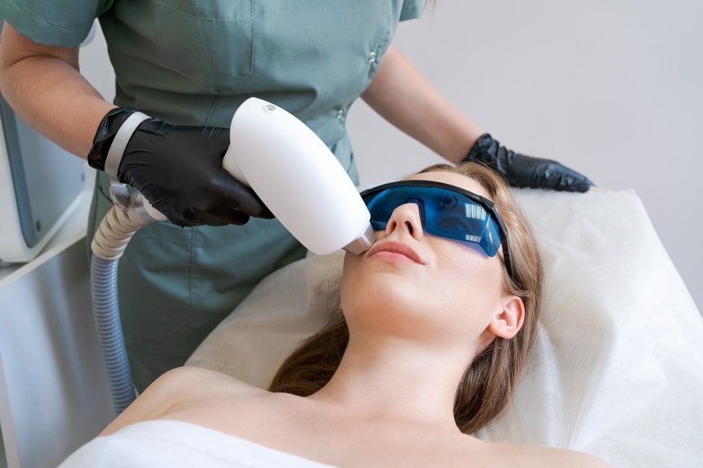 Therapist cosmetologist undergoes laser treatment on face young woman