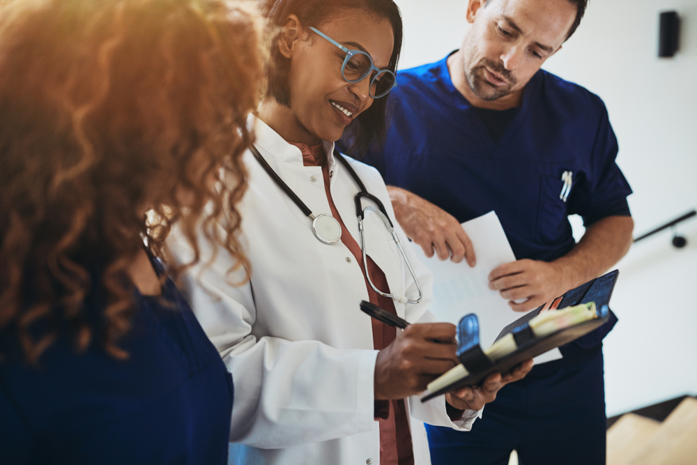 Smiling Group Of Diverse Doctors Reading A Patient's Notes Together