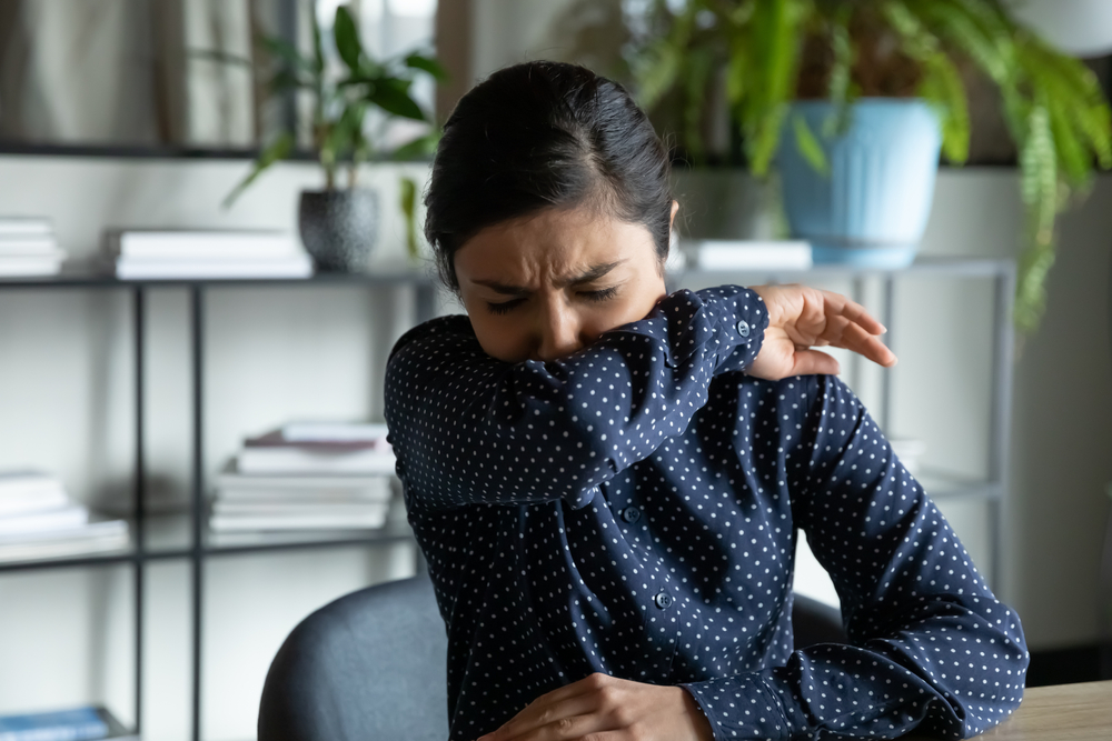 Millennial Indian Ethnic Girl Sitting In Office Coughing In Elbow