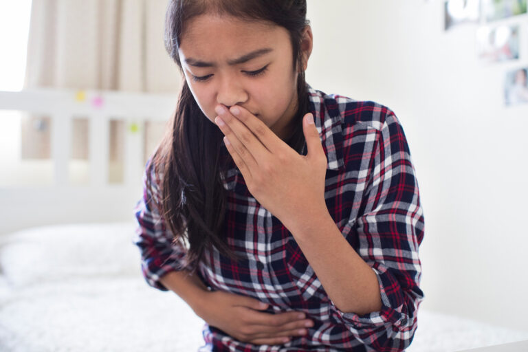 Young Girl Sitting On Bed At Home Feeling Nauseous