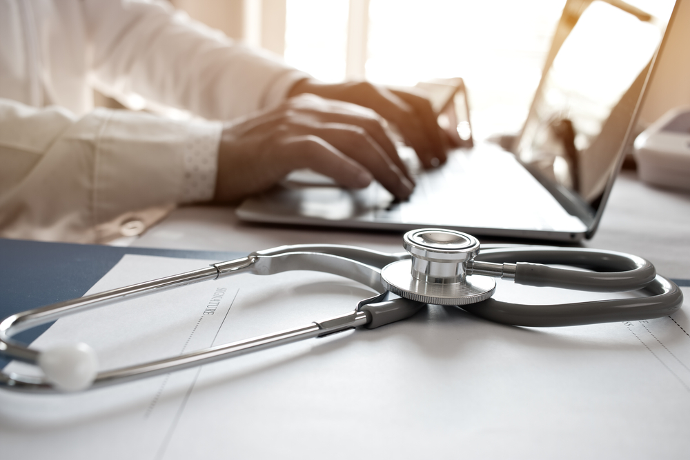 Doctor's Working On Laptop Computer Writing Prescription Clipboard With Record