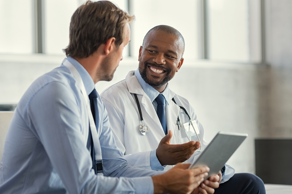 Two mature smiling doctors having discussion about patient diagnosis, holding digital tablet.