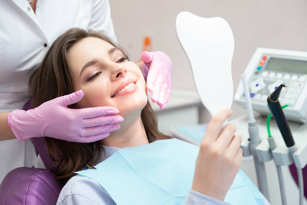 Smiling woman after teeth whitening procedure looking at mirror, caries treatment, toothache elimination