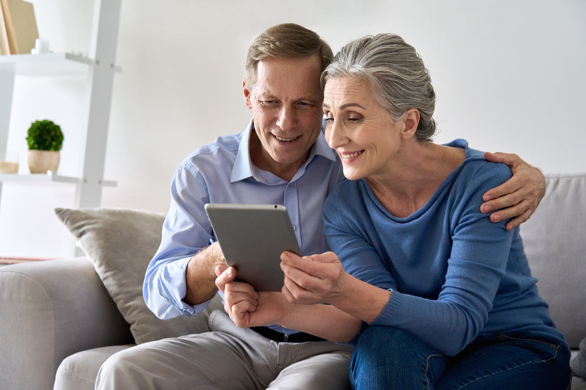 Happy old senior retired grandparents using digital tablet sitting on couch at home