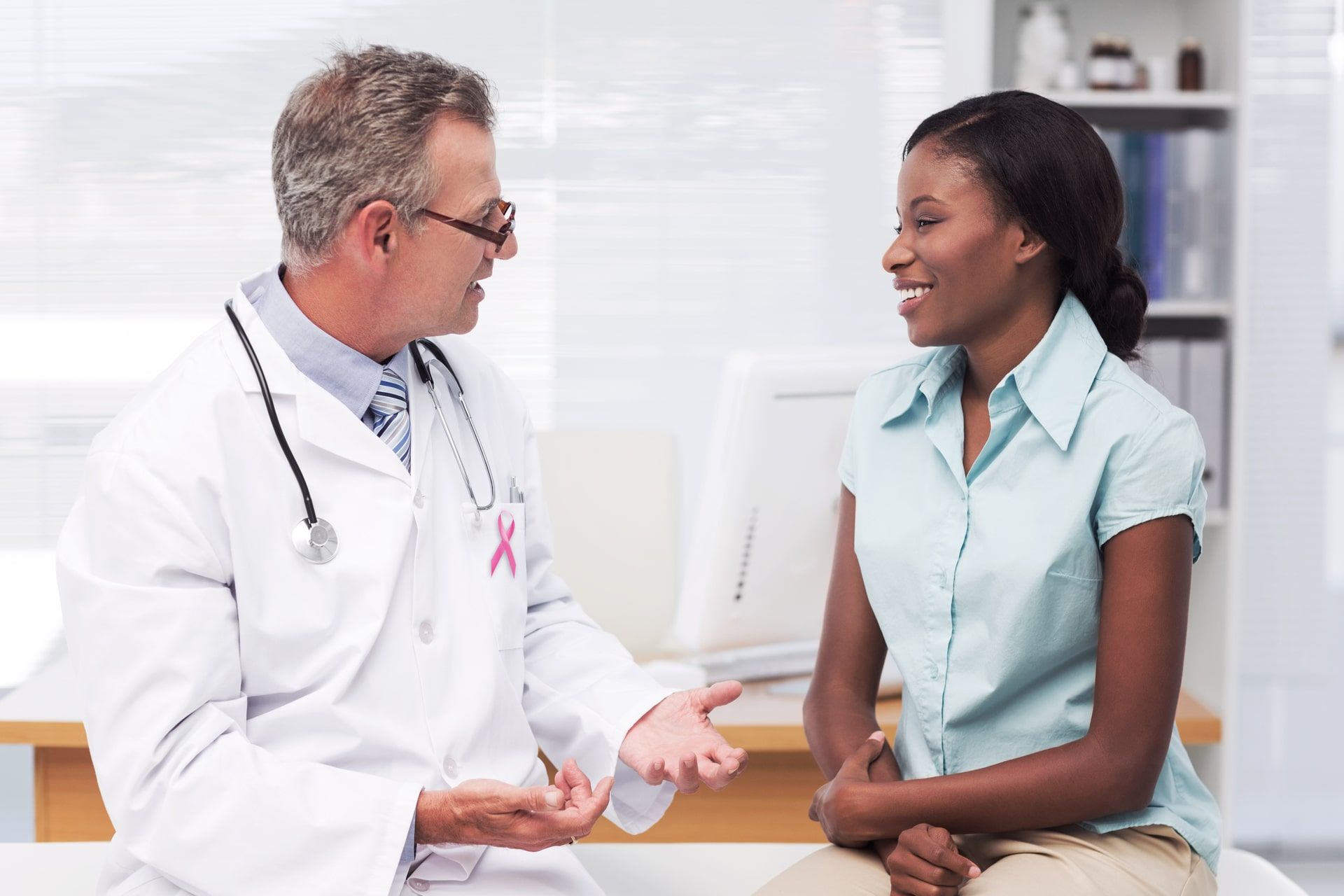 Pink awareness ribbon against doctor speaking with cheerful young patient