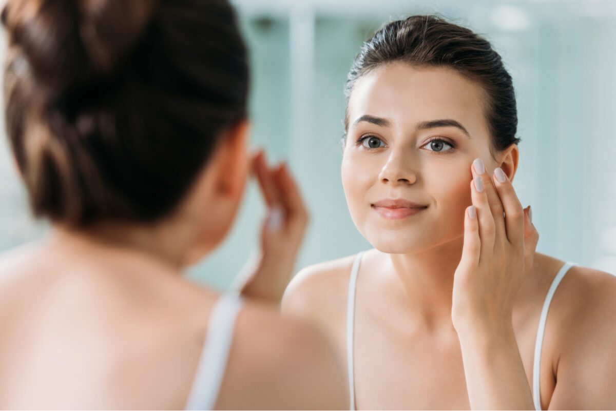 beautiful smiling girl touching face and looking at mirror in bathroom