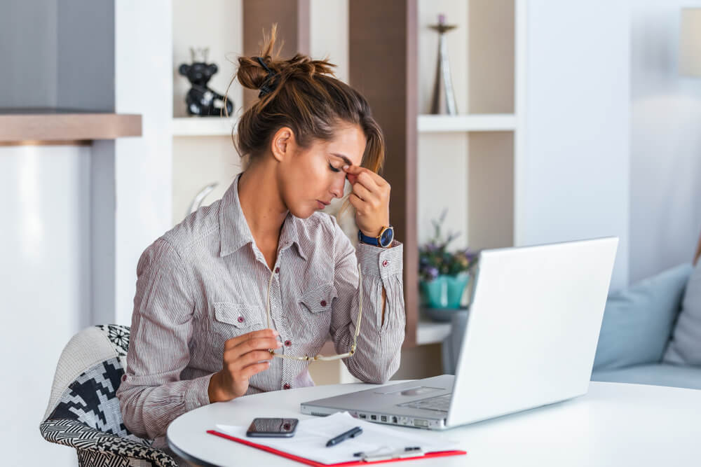 Young frustrated woman working at office desk in front of laptop