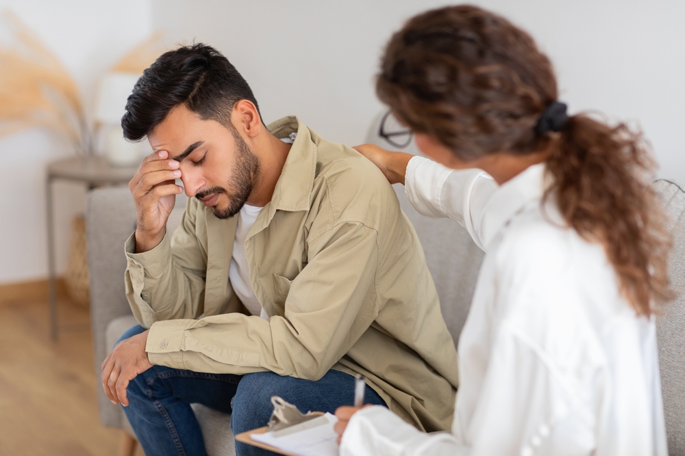 An adult man appears troubled requiring support as the woman therapist with notepad