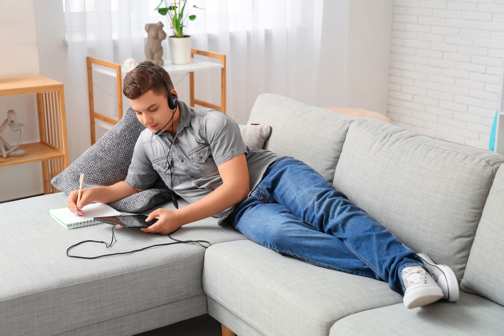 Teenage boy with headphones, tablet computer and notebook working at home