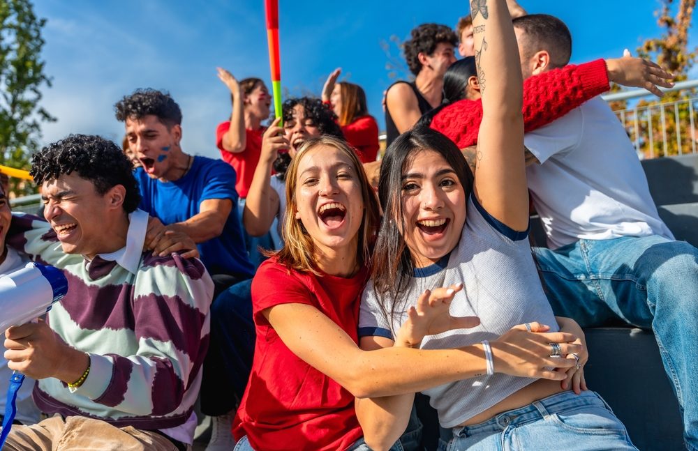 Cheerful young friends sitting in stadium stands
