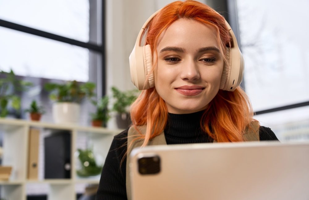 Young office worker with vibrant red hair smiles while using a tablet