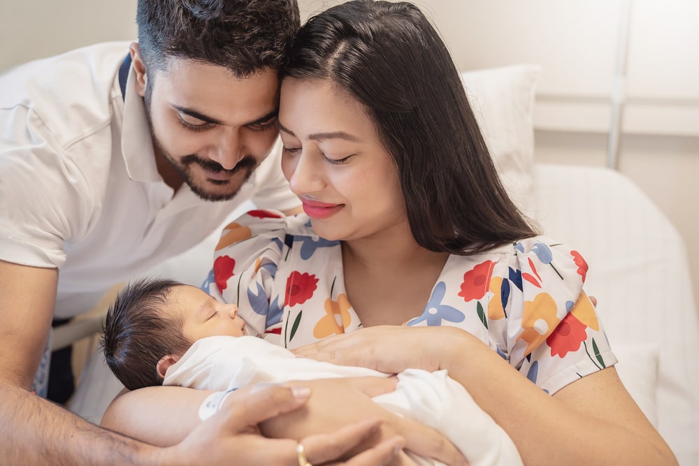 Young couple father mother holding new born baby in hospital bed