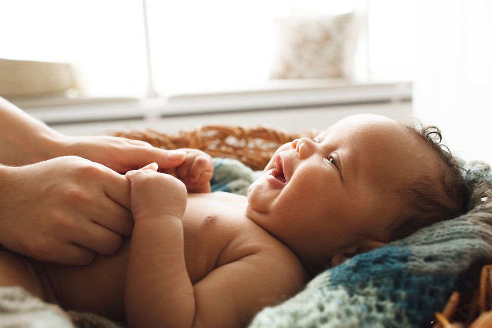 Adorable newborn child looking up at mother and holding her hands.