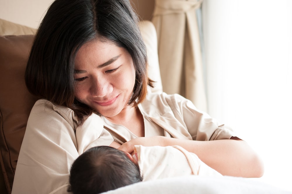 Mother breastfeeding her newborn baby beside window