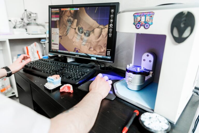 Dental technician using software to design teeth and prosthetics with models and scanner.