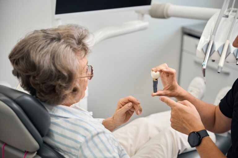 Doctor shows a model of dental implant to elderly lady