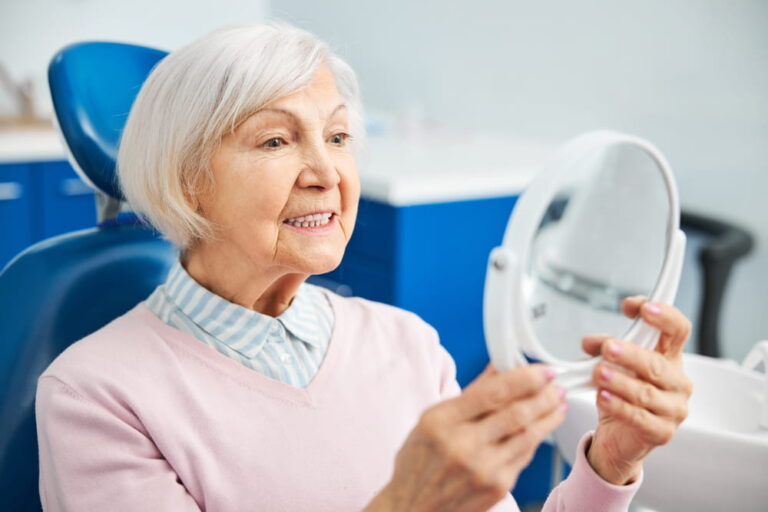 Focused aging female raising table mirror to see teeth