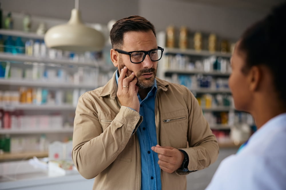 Mid adult man with toothache talking to a pharmacist in drugstore.